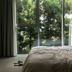 a bed sitting in front of a window next to a pair of shoes on the floor