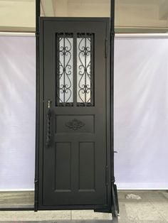 a black front door with glass panels and wrought iron design on the side walk way