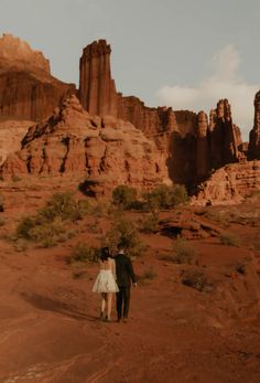 a man and woman are walking through the desert with red rocks in the back ground