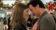 a man and woman standing next to each other in front of a christmas tree with lights