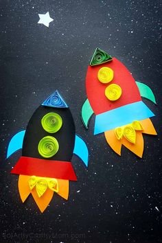 two paper rockets sitting on top of a black surface with stars in the sky behind them