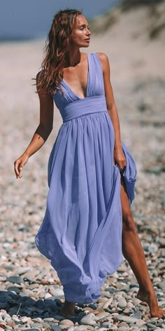 a woman in a blue dress is walking on the rocky beach with her legs spread out