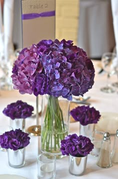 purple flowers are in vases on a white table cloth at a formal dinner event