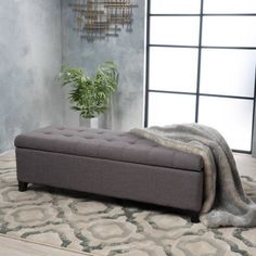 a gray bench sitting on top of a rug next to a plant in a vase