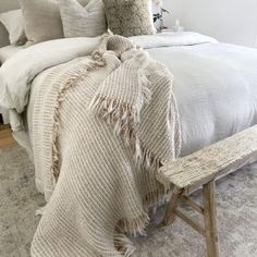 a bed with white linens and pillows in a bedroom next to a wooden bench