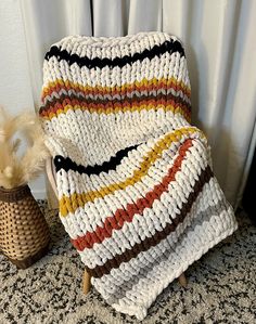 a knitted blanket sitting on top of a wooden chair next to a basket with feathers