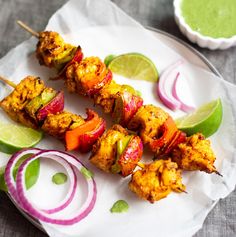 chicken kabobs with onions and limes on a white plate