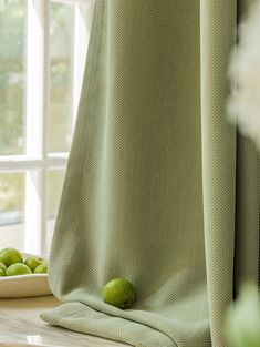 the green apples are sitting on the table by the window in front of the curtain