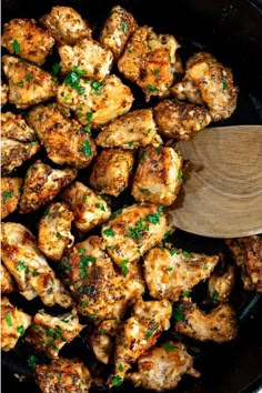 chicken is being cooked in a skillet with a wooden spoon on the side, and garnished with parsley