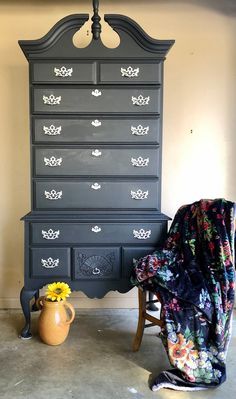 an old dresser has been painted black with flowers on it and is next to a chair