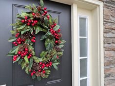 a christmas wreath on the front door of a house with pine cones, holly and red berries