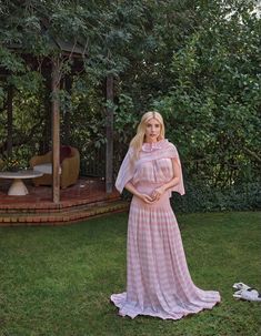 a woman in a pink and white dress standing next to a gazebo on the grass