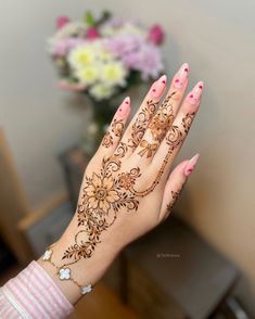 a woman's hand with henna tattoos on it and flowers in the background