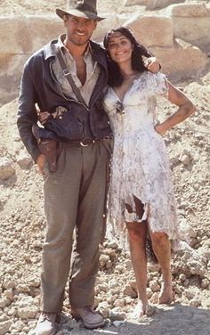 a man and woman standing next to each other in front of some rocks on the ground