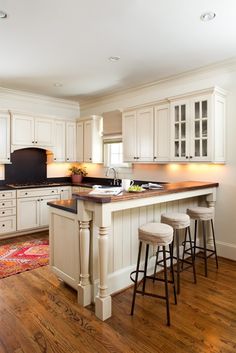 a large kitchen with white cabinets and black counter tops is pictured in this image, the island has four stools on it