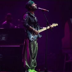 a man standing in front of a microphone while holding a guitar