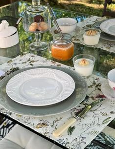 a glass table topped with plates and bowls filled with food next to a jar of orange juice