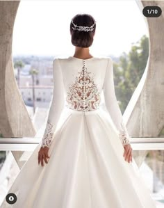 a woman in a white wedding dress looking out the window with her hands on her hips