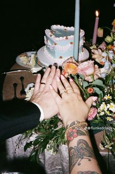 two people holding hands over a table with cake and flowers on it, surrounded by candles