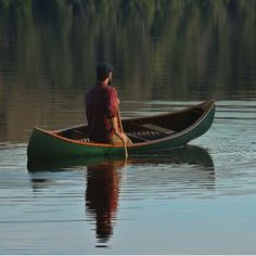 a man sitting in a green canoe on top of a body of water with trees in the background