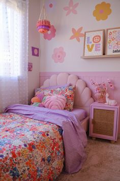 a bedroom decorated in pink, yellow and purple with flowers on the wall above the bed