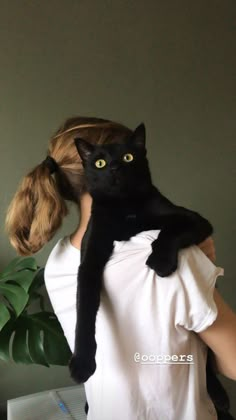 a woman is holding a black cat in her arms while wearing a white t - shirt