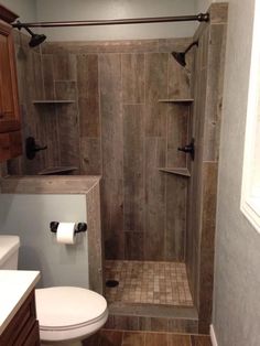 a walk in shower sitting next to a white toilet and wooden cabinetry on the wall