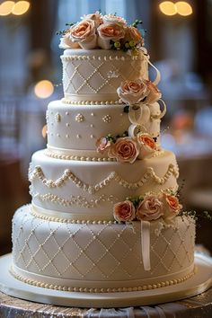 a three tiered wedding cake with roses on top and pearls around the edges, sitting on a table