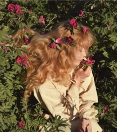 a woman with long red hair sitting in the middle of pink flowers on her head