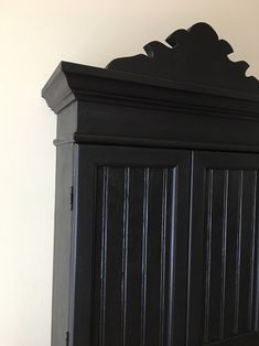 a black armoire sitting on top of a wooden floor next to a white wall