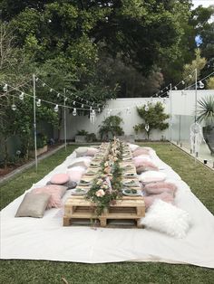 a long table is set up in the backyard for an outdoor party with pink and white pillows