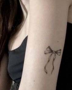 a woman's arm with a bow tattoo on the left side of her arm