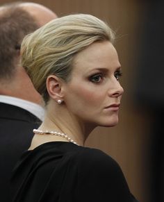 a woman with blonde hair wearing a black dress and pearls on her neck, looking off to the side