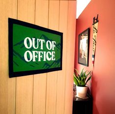 there is a sign that says out of office on the wall next to a potted plant