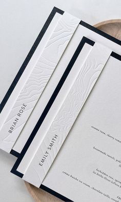 two white and black wedding cards on top of a wooden plate next to each other