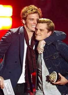 two men standing next to each other on stage with one holding an award in his hand