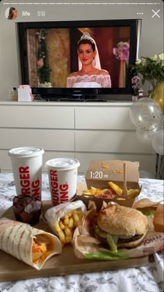 a tray with sandwiches, french fries and drinks on it in front of a flat screen tv