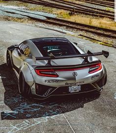 the rear end of a silver sports car parked in front of train tracks with graffiti on it