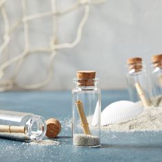 three bottles filled with sand and wooden spoons on top of a blue tablecloth