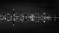 black and white photo of the city skyline at night with lights reflecting in the water