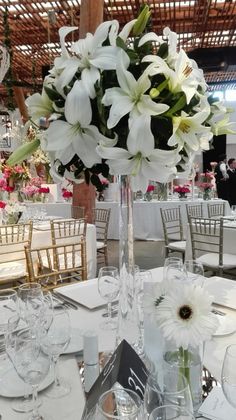 white flowers are in a tall glass vase on the center table at a wedding reception