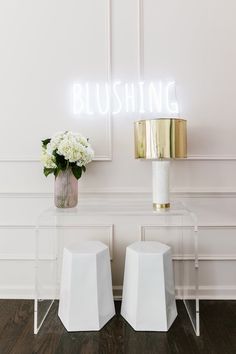 two white stools sitting next to each other in front of a wall with a neon sign