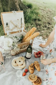 a woman sitting at a picnic table with food and wine in front of an open suitcase