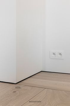 an empty room with white walls and wood flooring in front of a light switch