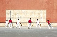 four men in white and red uniforms are playing tennis on the pavement near a brick wall