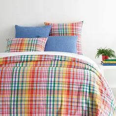 a bed with colorful plaid sheets and pillows on top of it next to a potted plant