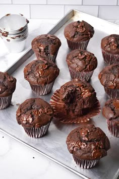 chocolate muffins sitting on top of a metal tray next to a cupcake tin