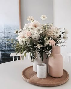 two vases with flowers in them sitting on a wooden tray next to the ocean