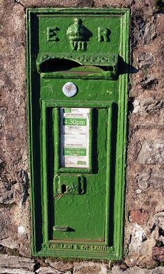 a green mailbox on the side of a stone wall