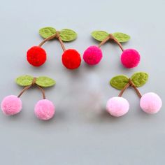 four cherries with green leaves and pink pom - poms are arranged on a gray surface